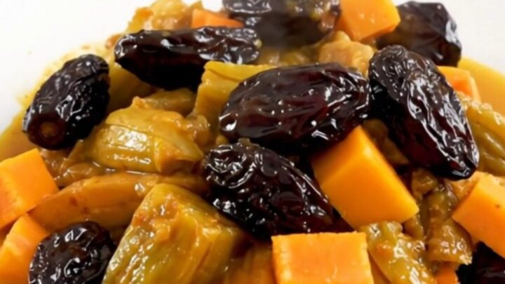 A steaming, glossy vegetarian tagine with squash, carrots, and prunes served on a white plate.