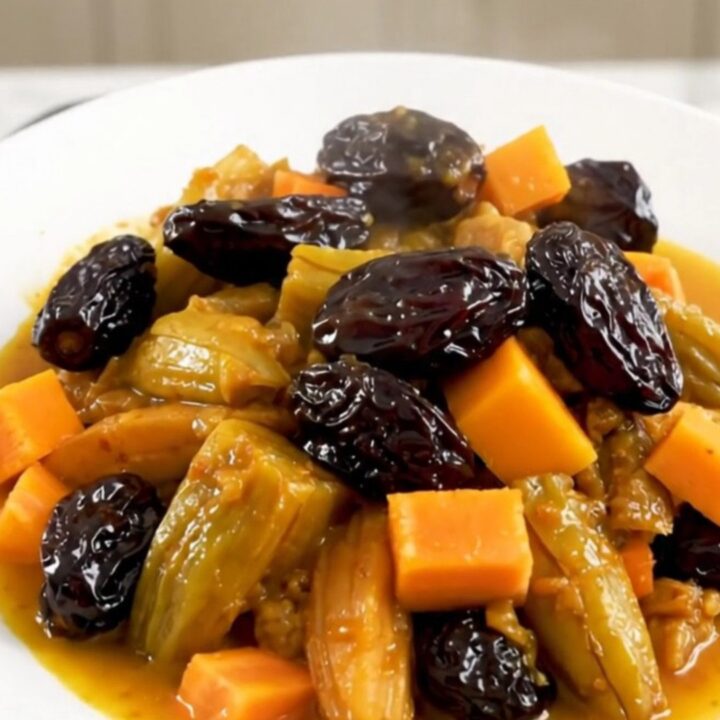 A steaming, glossy vegetarian tagine with squash, carrots, and prunes served on a white plate.