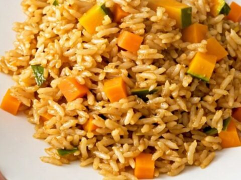 A top-down view of a steaming, golden-hued autumn vegetable pilaf served on a clean, round white plate.