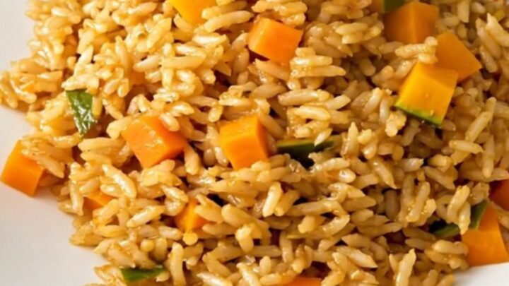 A top-down view of a steaming, golden-hued autumn vegetable pilaf served on a clean, round white plate.