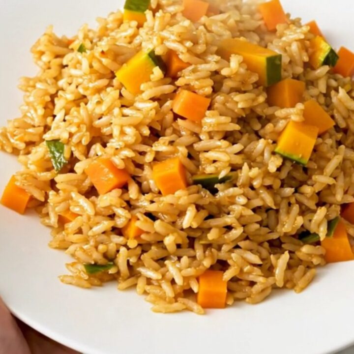 A top-down view of a steaming, golden-hued autumn vegetable pilaf served on a clean, round white plate.