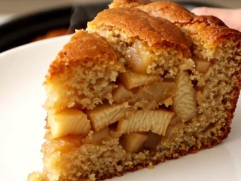 Gâteau aux pommes doré et fondant, servi dans une assiette blanche avec des reflets de lumière naturelle.