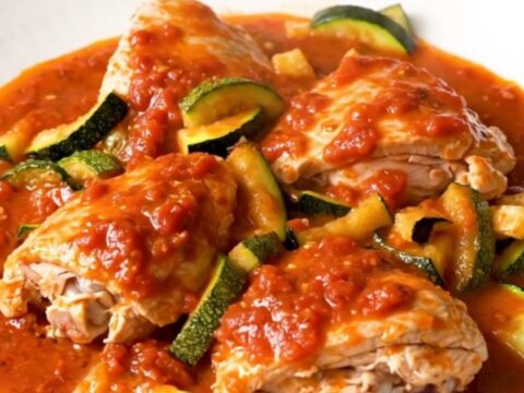A close-up of slow-cooked Provencal chicken and zucchini served on a white plate with tomato sauce.