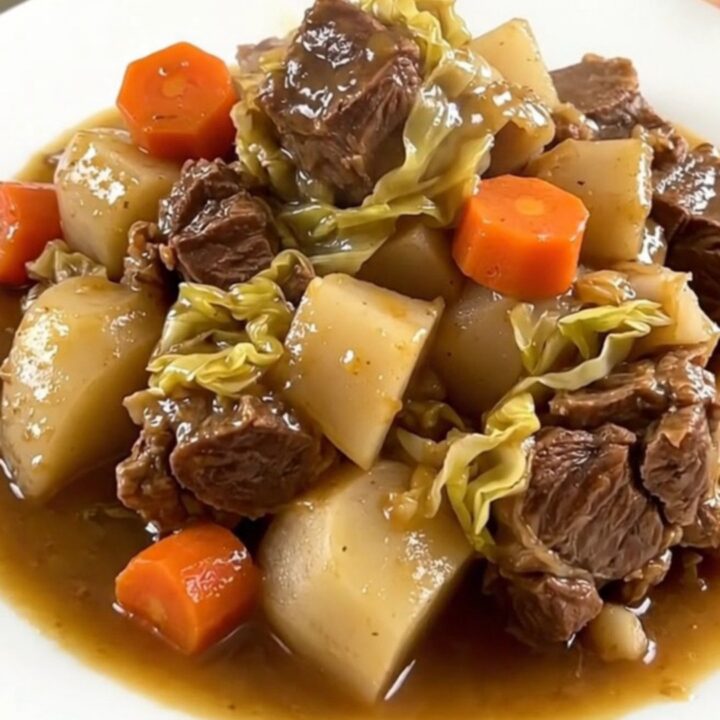 A rustic slow cooker filled with chunks of pork belly, beef, carrots, turnips, and cabbage in a savory broth.
