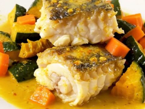 A top-down view into a slow cooker filled with monkfish, autumn vegetables, and a creamy saffron sauce.