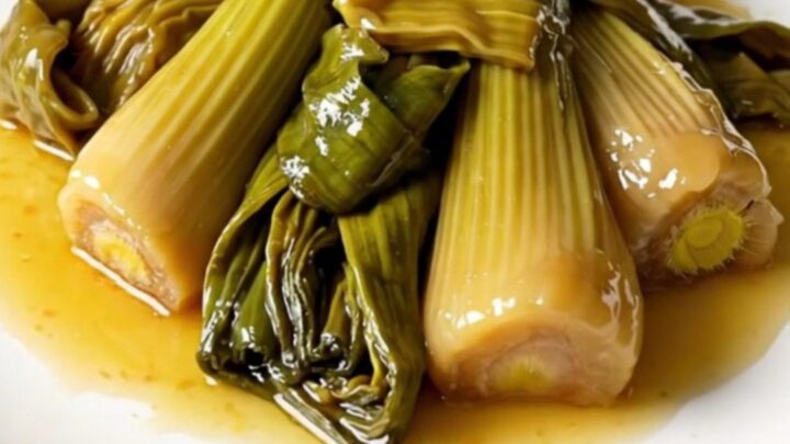 A close-up overhead shot of braised leeks in a white wine and mustard sauce inside a black slow cooker.