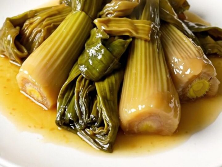 A close-up overhead shot of braised leeks in a white wine and mustard sauce inside a black slow cooker.