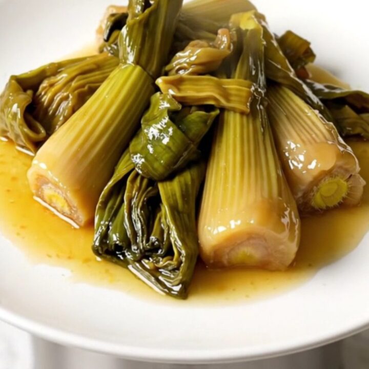 A close-up overhead shot of braised leeks in a white wine and mustard sauce inside a black slow cooker.