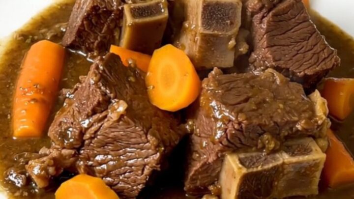 A close-up of tender beef neck stew with vibrant yellow carrots in a black slow cooker.