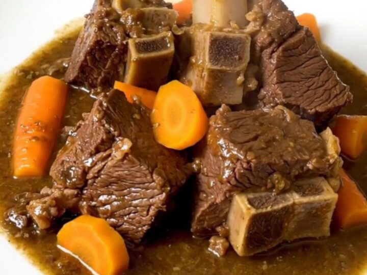 A close-up of tender beef neck stew with vibrant yellow carrots in a black slow cooker.