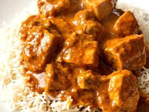 A top-down view of creamy slow cooker butter chicken served over white rice on a clean white plate.