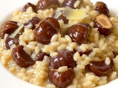A top-down view of a black slow cooker filled with creamy chestnut and parmesan risotto on a white speckled countertop.