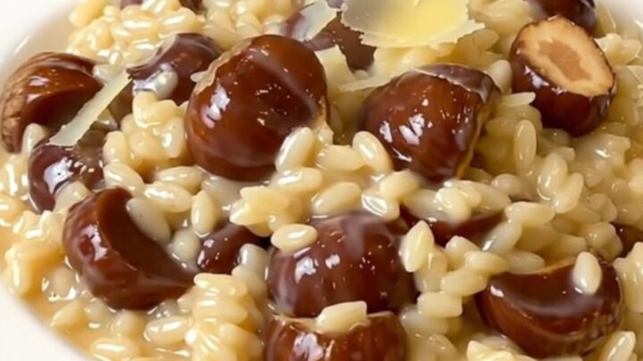 A top-down view of a black slow cooker filled with creamy chestnut and parmesan risotto on a white speckled countertop.