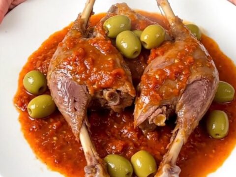 A plate of tender braised duck legs covered in a rich tomato and green olive sauce, ready to serve.