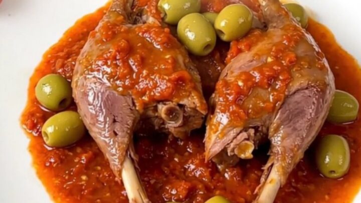 A plate of tender braised duck legs covered in a rich tomato and green olive sauce, ready to serve.