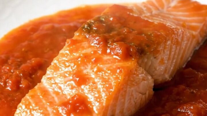 A close-up view of cooked salmon fillets topped with tomato coulis and onions in a slow cooker.