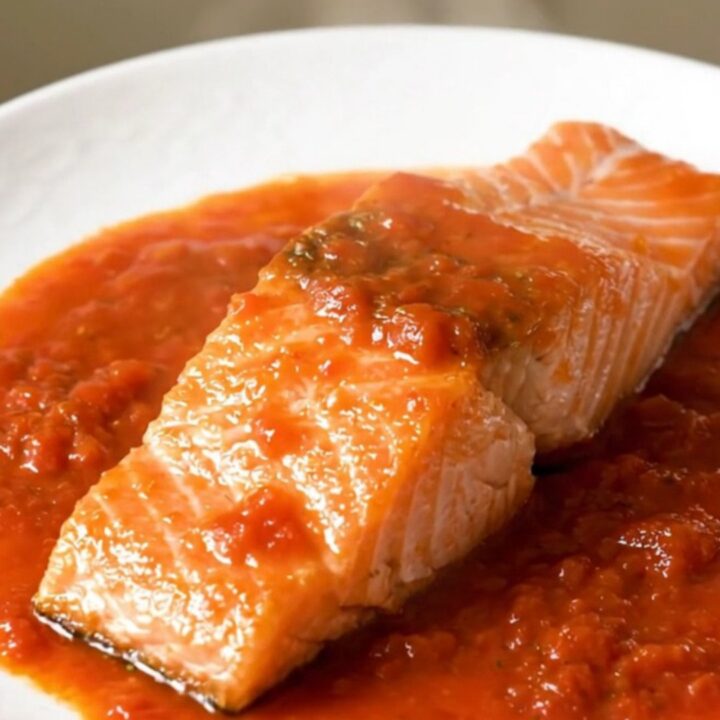 A close-up view of cooked salmon fillets topped with tomato coulis and onions in a slow cooker.