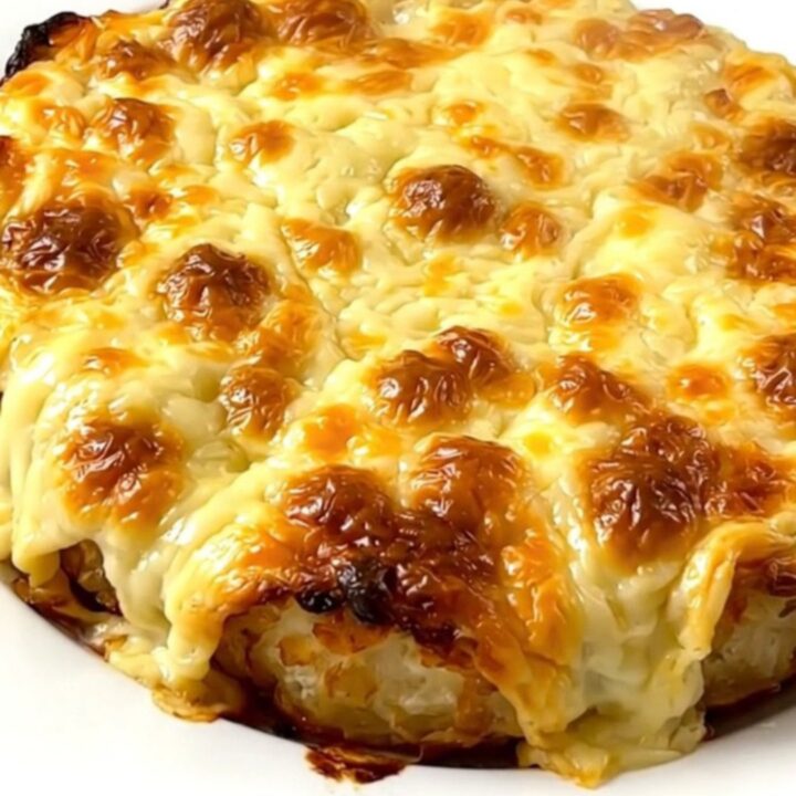A steaming, creamy Munster tartiflette served on a white plate with melted cheese and visible cumin seeds.