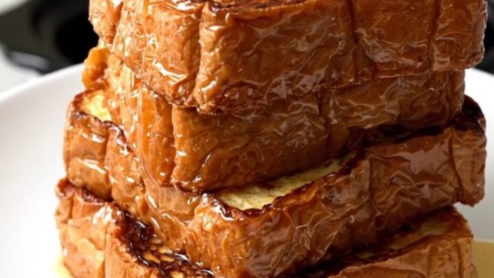 A close-up of golden, glossy brioche French toast served on a white plate in a bright kitchen.