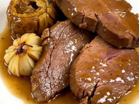 Slow cooked veal shoulder with garlic confit in a black slow cooker on a quartz countertop.