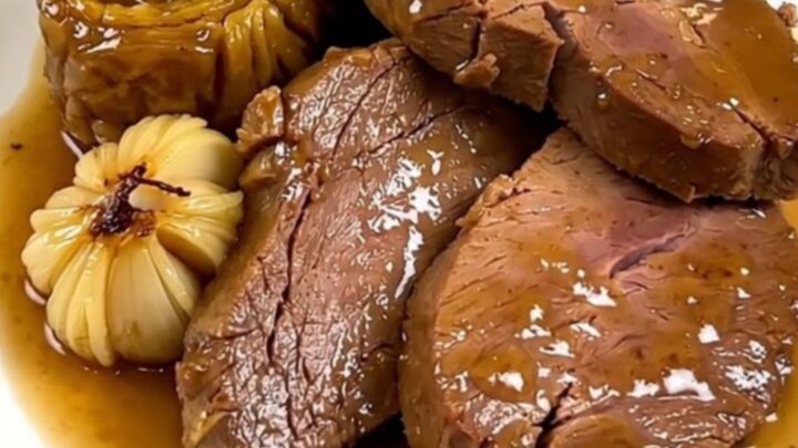 Slow cooked veal shoulder with garlic confit in a black slow cooker on a quartz countertop.