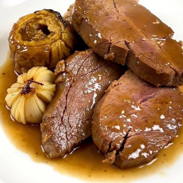 Slow cooked veal shoulder with garlic confit in a black slow cooker on a quartz countertop.