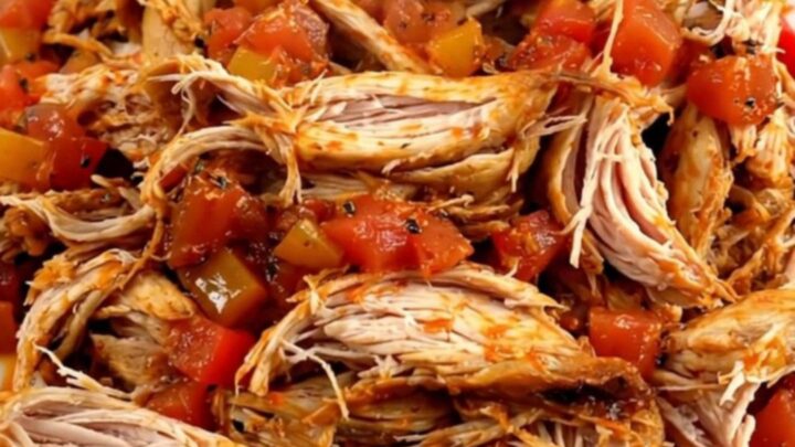 A top-down view of a black slow cooker filled with raw chicken, bell peppers, onions, and crushed tomatoes.