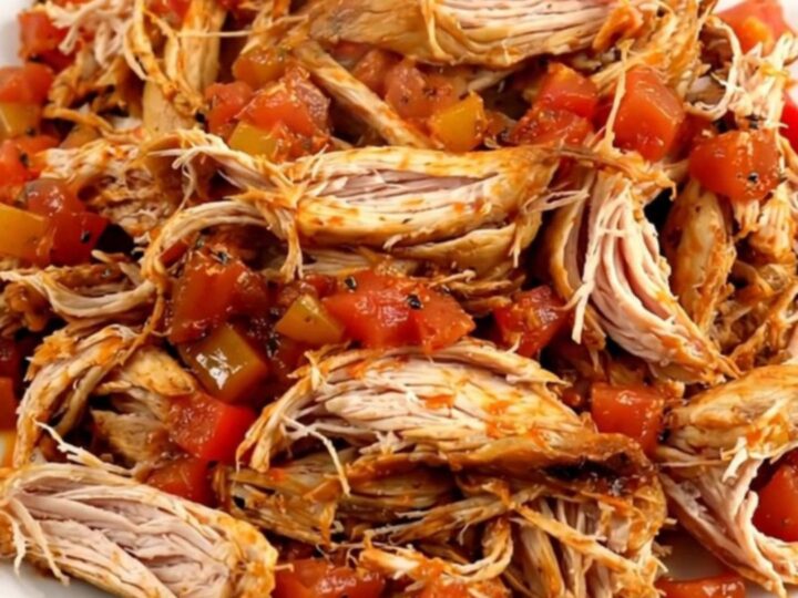 A top-down view of a black slow cooker filled with raw chicken, bell peppers, onions, and crushed tomatoes.