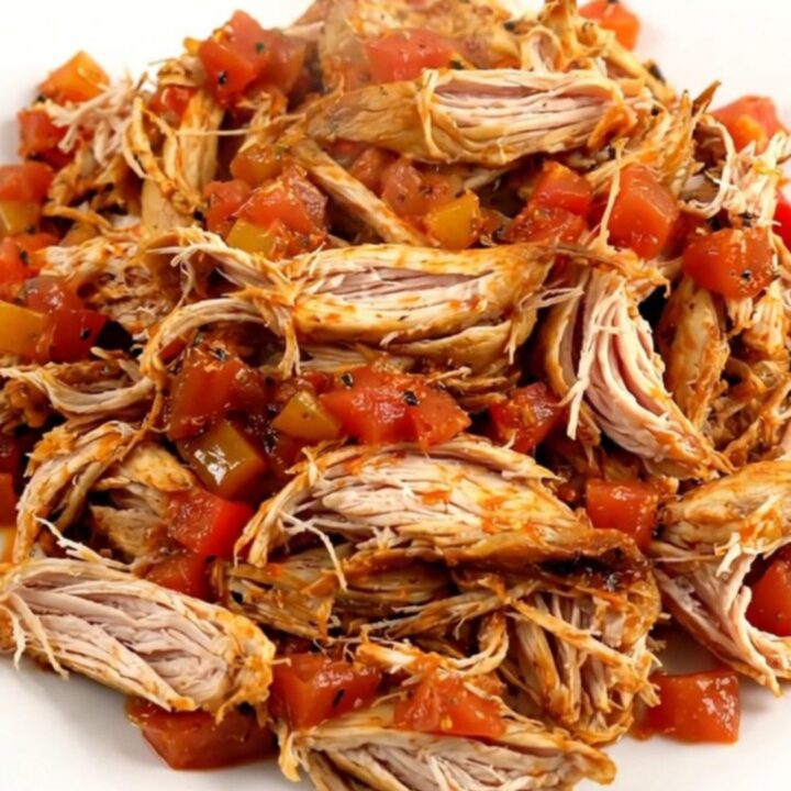 A top-down view of a black slow cooker filled with raw chicken, bell peppers, onions, and crushed tomatoes.