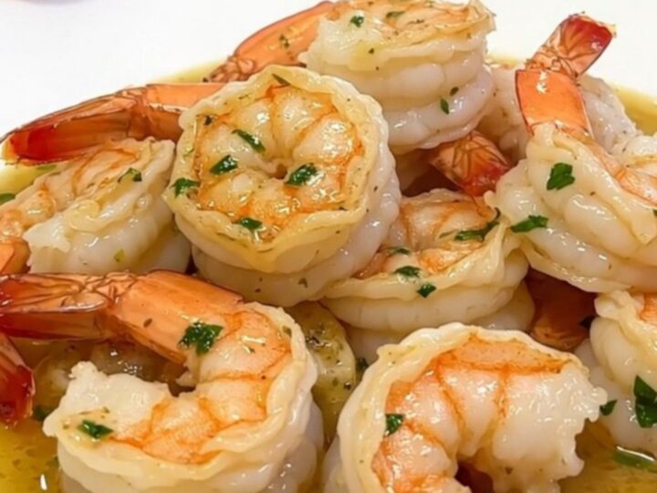 A top-down view of raw shrimp, parsley, garlic, and cream inside a black slow cooker insert.