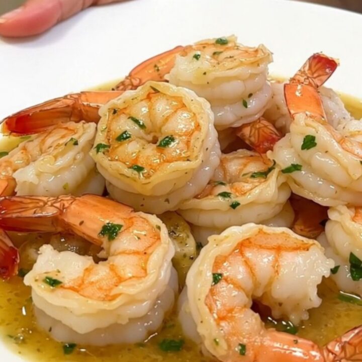 A top-down view of raw shrimp, parsley, garlic, and cream inside a black slow cooker insert.