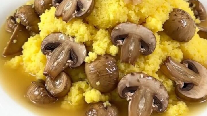 A close-up of a creamy parmesan polenta dish with mushrooms served in a white bowl with a garnish.