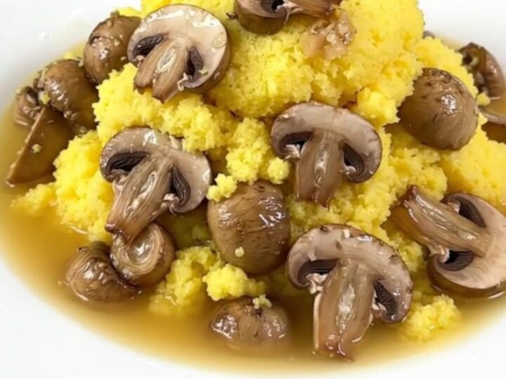 A close-up of a creamy parmesan polenta dish with mushrooms served in a white bowl with a garnish.