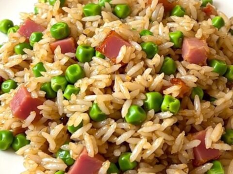 A top-down view of a black slow cooker filled with white rice, peas, and ham, ready for cooking.