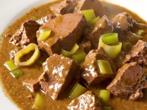 A close-up of creamy mustard veal stew with leeks served in a white bowl.