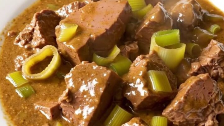 A close-up of creamy mustard veal stew with leeks served in a white bowl.