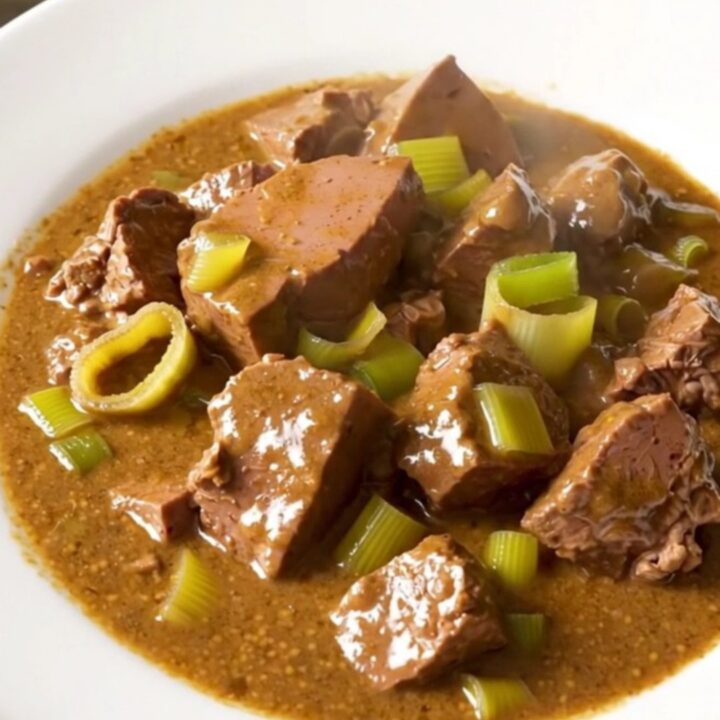 A close-up of creamy mustard veal stew with leeks served in a white bowl.