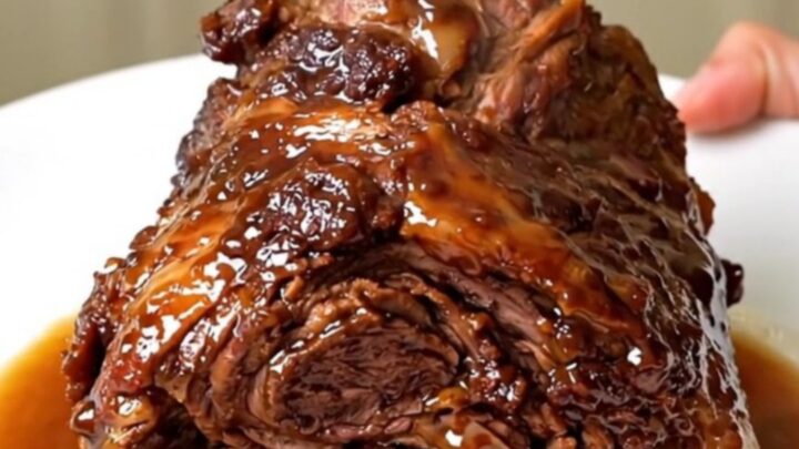 A slow cooker filled with a tender, spiced lamb shoulder and red onions on a white quartz countertop.