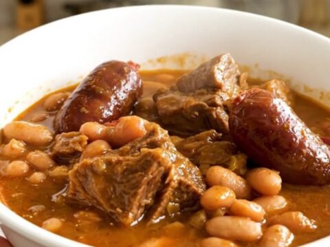 A rustic slow cooker cassoulet served in a white bowl showing chunks of tender pork and sausages.