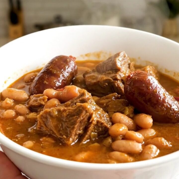 A rustic slow cooker cassoulet served in a white bowl showing chunks of tender pork and sausages.
