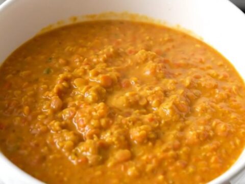 A white bowl filled with creamy yellow coconut red lentil dahl, steaming and garnished lightly.