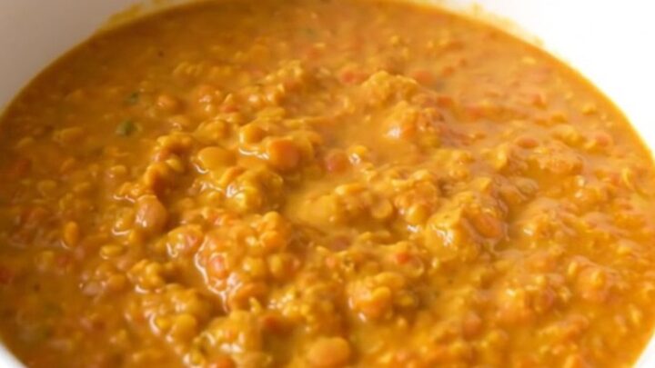 A white bowl filled with creamy yellow coconut red lentil dahl, steaming and garnished lightly.