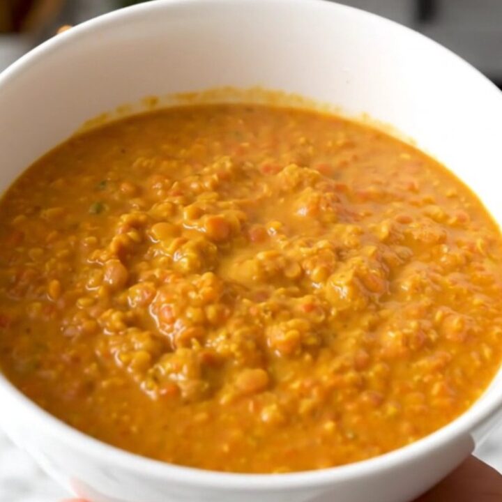A white bowl filled with creamy yellow coconut red lentil dahl, steaming and garnished lightly.