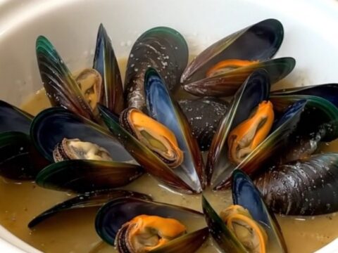 A slow cooker filled with steaming mussels, leeks, and a savory blonde beer broth on a white quartz countertop.