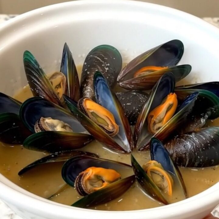 A slow cooker filled with steaming mussels, leeks, and a savory blonde beer broth on a white quartz countertop.