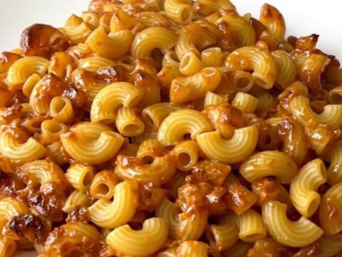 A close-up of creamy mac and cheese in a slow cooker with visible melted cheese and herbs.