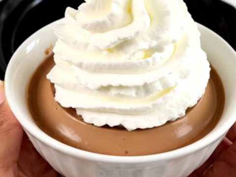 A glossy coffee crème liégeoise served in a white bowl with a generous swirl of whipped cream on top.
