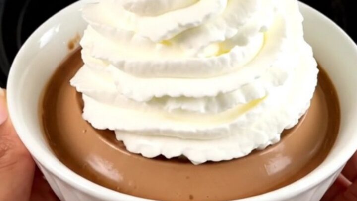 A glossy coffee crème liégeoise served in a white bowl with a generous swirl of whipped cream on top.