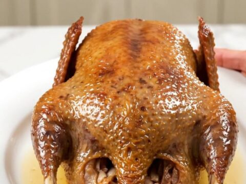 A whole, golden-roasted guinea fowl resting on a white plate with fresh thyme and caramelized garlic.