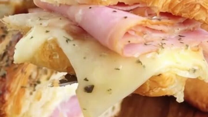 A warm, buttery croissant sandwich filled with layers of ham and melted Swiss cheese, held up for a close-up.